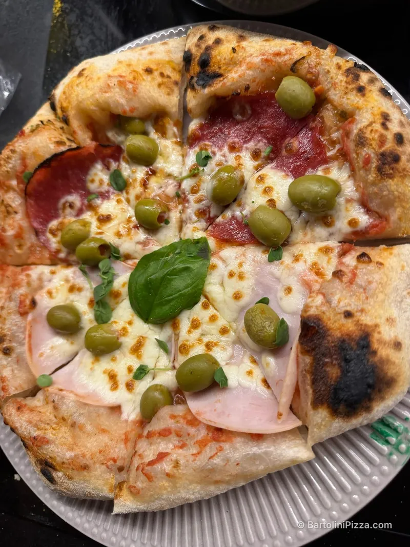 Pokrojona pizza z oliwkami, szynką, salami i bazylią na talerzu.