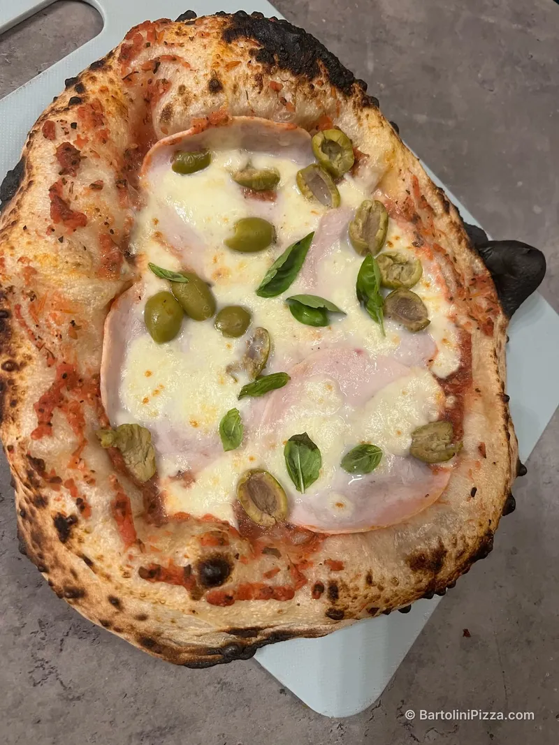 Pizza neapolitańska z szynką, zielonymi oliwkami i bazylią, widok z góry.
