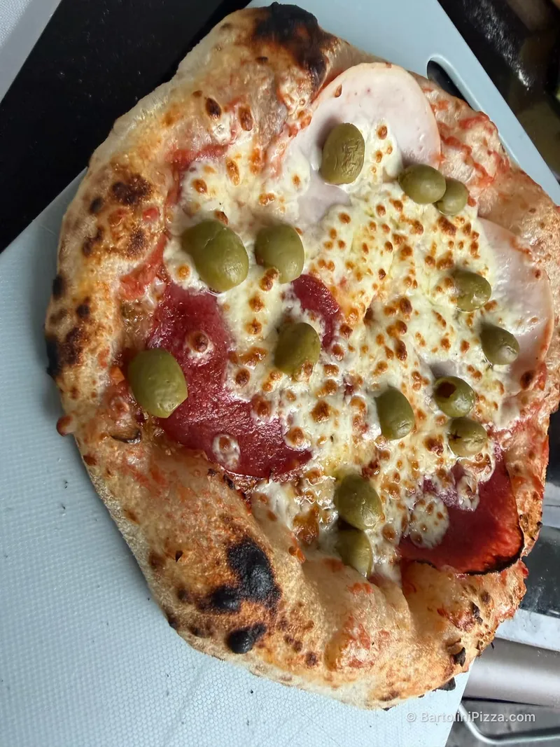 Pizza z salami, szynką i zielonymi oliwkami, z przypieczonym brzegiem.