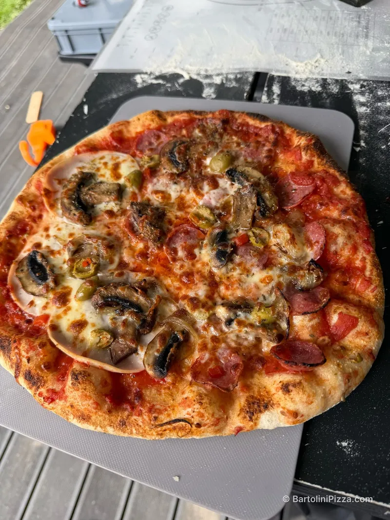 Duża pizza z pieczarkami, salami i oliwkami na kamieniu do pieczenia.